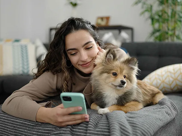Frau mit Hund hält ein Handy in der Hand